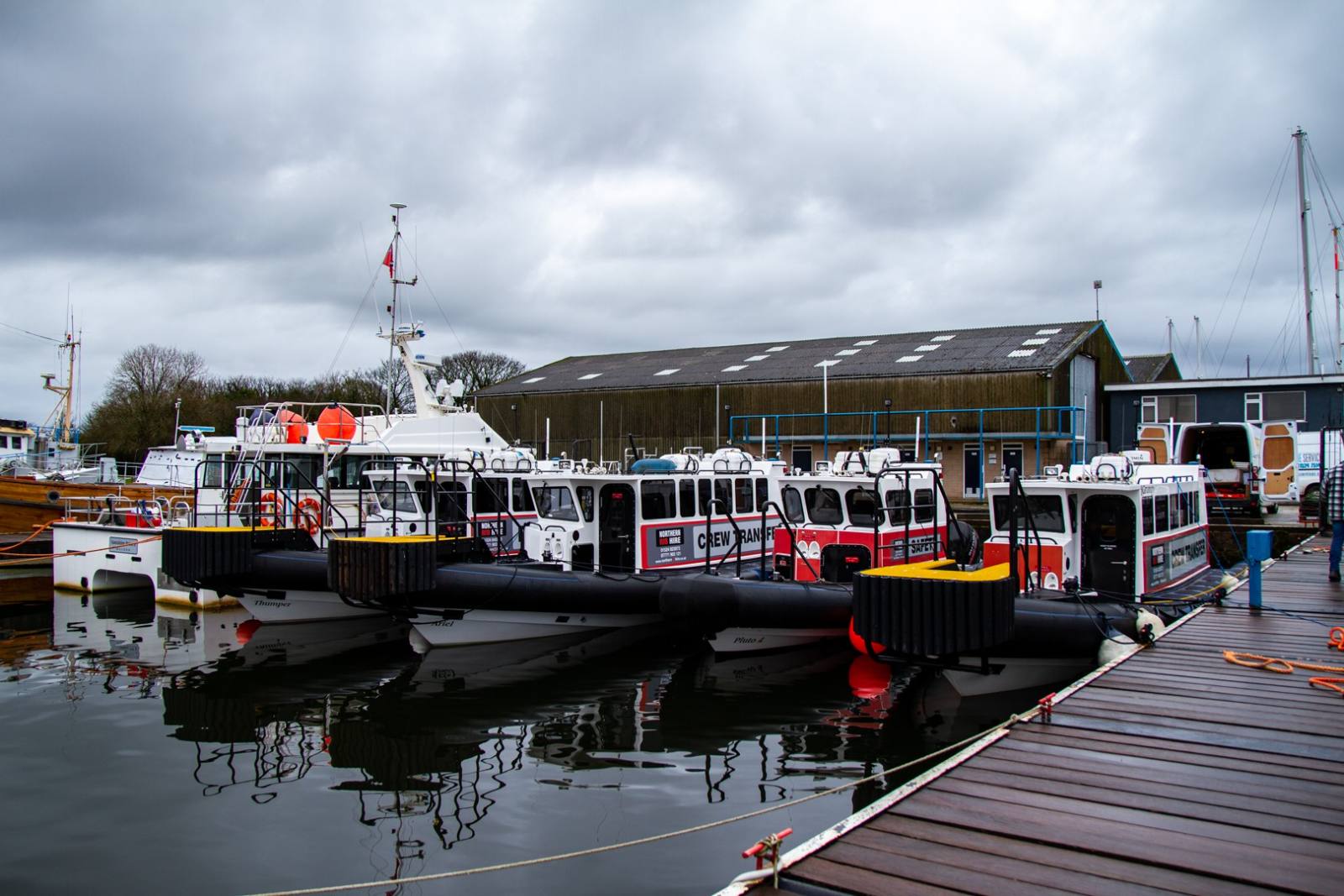 Fleet of crew transfer boats moored alongside a working boatyard